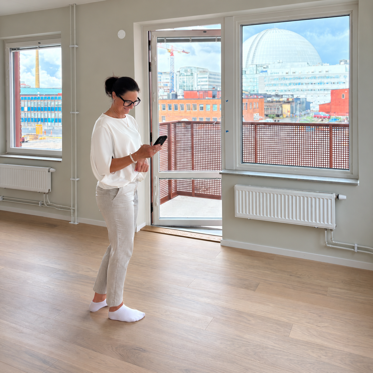 Maria använder mobilen i en ljus bostad med Globen synlig genom fönstret.
