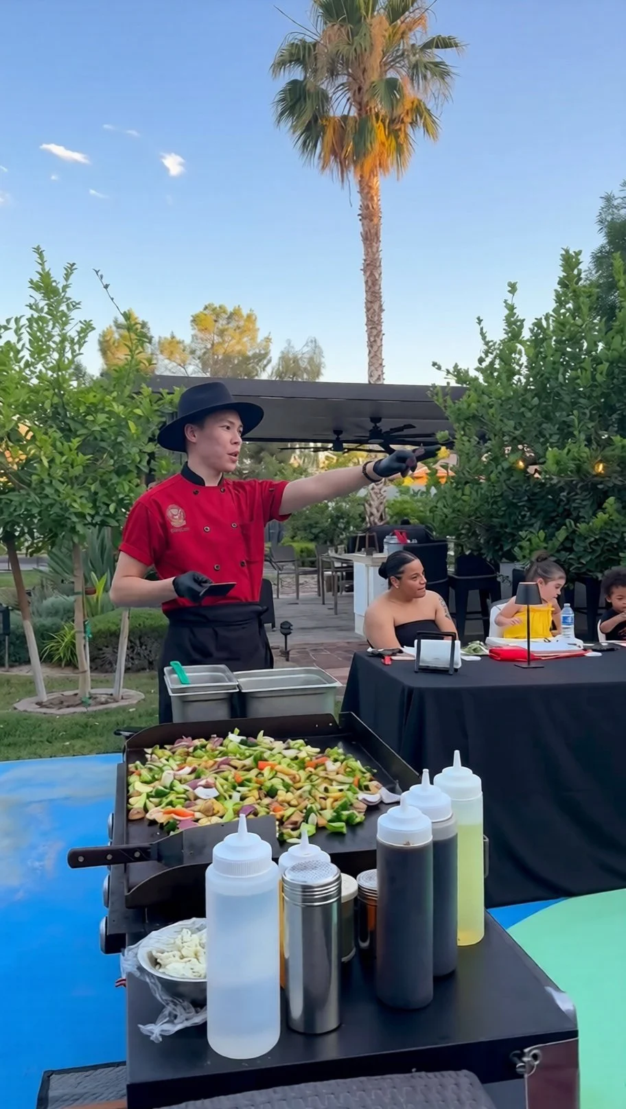 Private hibachi chef cooking at grill with palm trees and guests in the background, Los Angeles