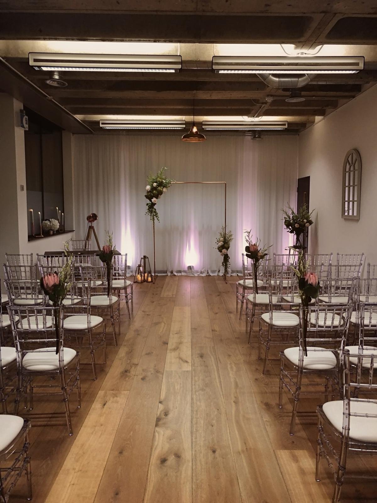 Rows of clear chairs with proteas lining the aisle to a copper arch