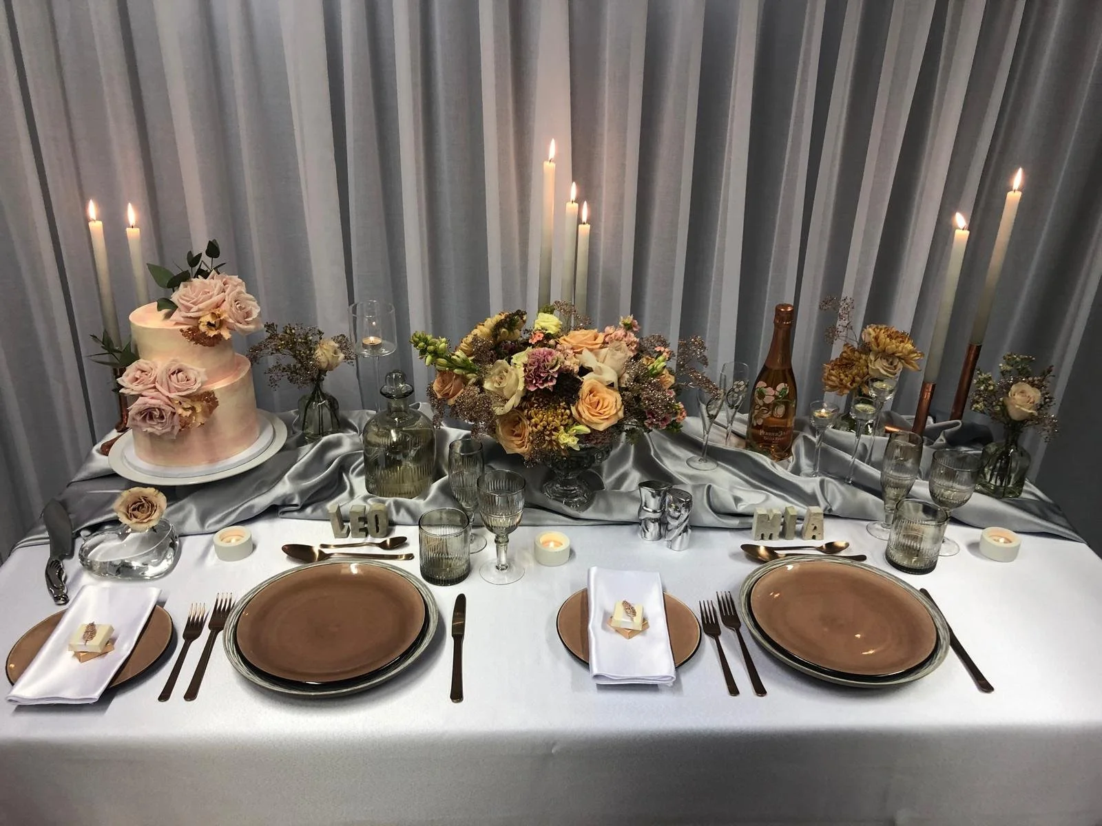 A top table set with blush plates, copper cutlery, candles and a rose cake
