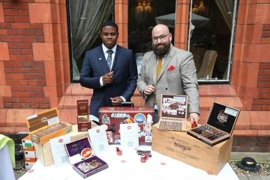 Hosts beside a display of cigar boxes on the terrace