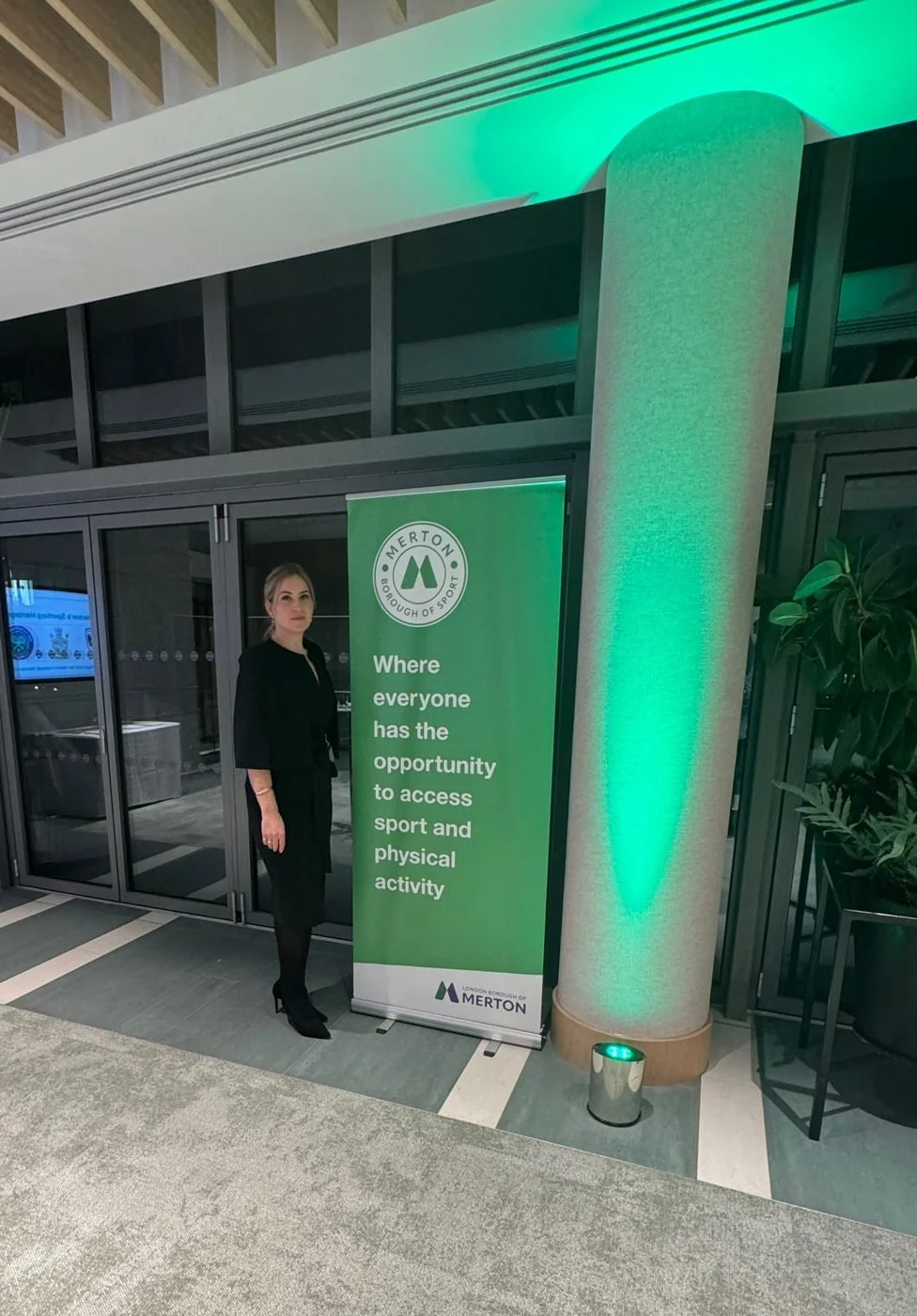 Layla beside a Merton Borough of Sport banner under green uplighting