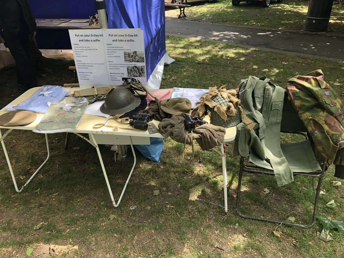 A table of wartime uniforms, helmets and binoculars with a sign inviting visitors to try on D-Day kit