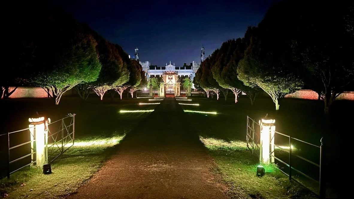 A lit avenue of trees leading to the house at night