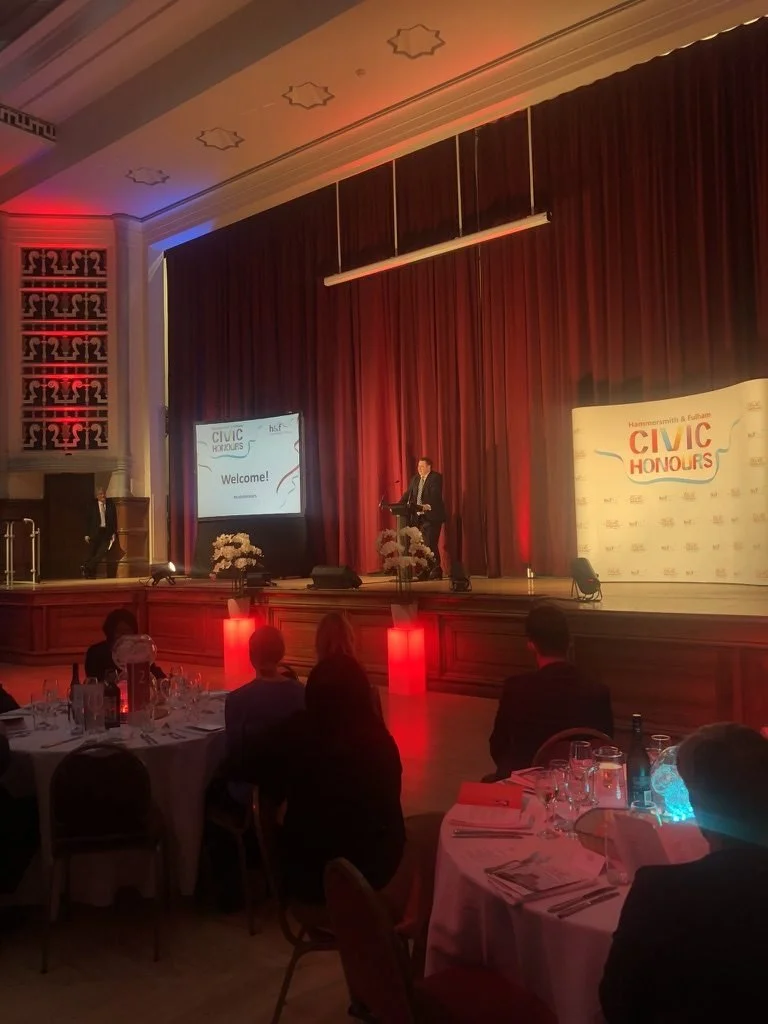 A speaker on stage at the Civic Honours awards evening with red uplighting and dressed tables