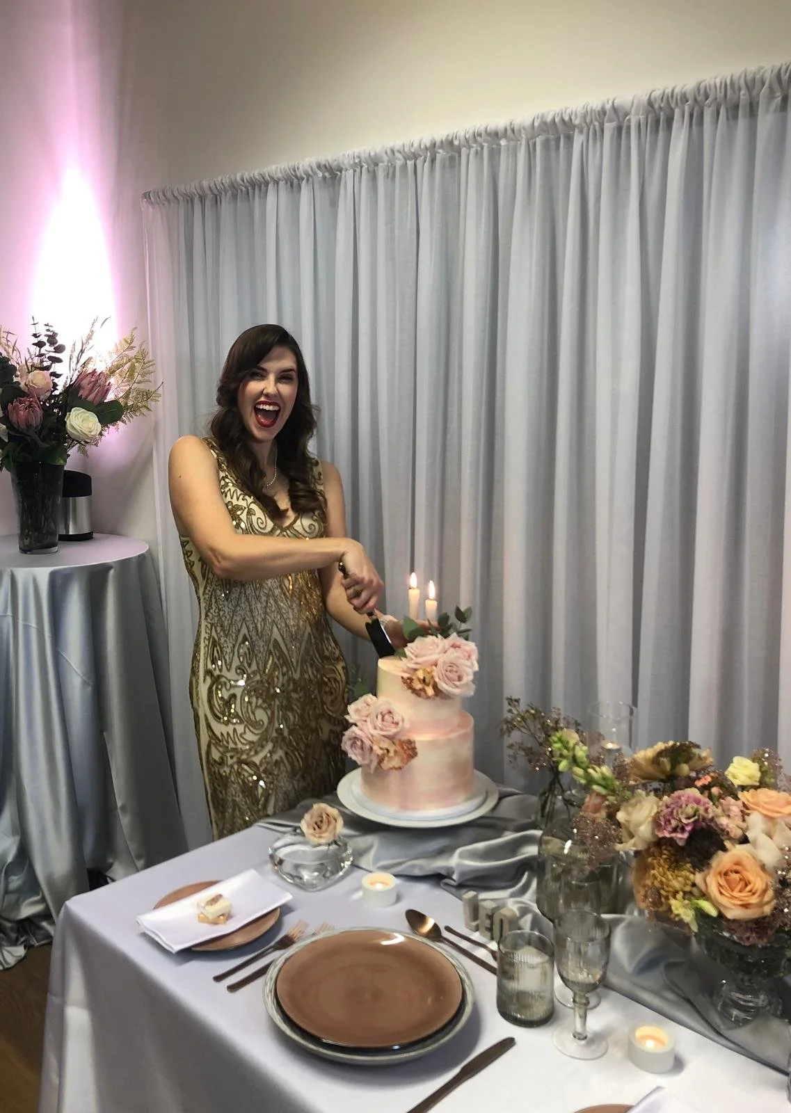A guest in a gold sequinned dress laughing as she cuts the rose cake