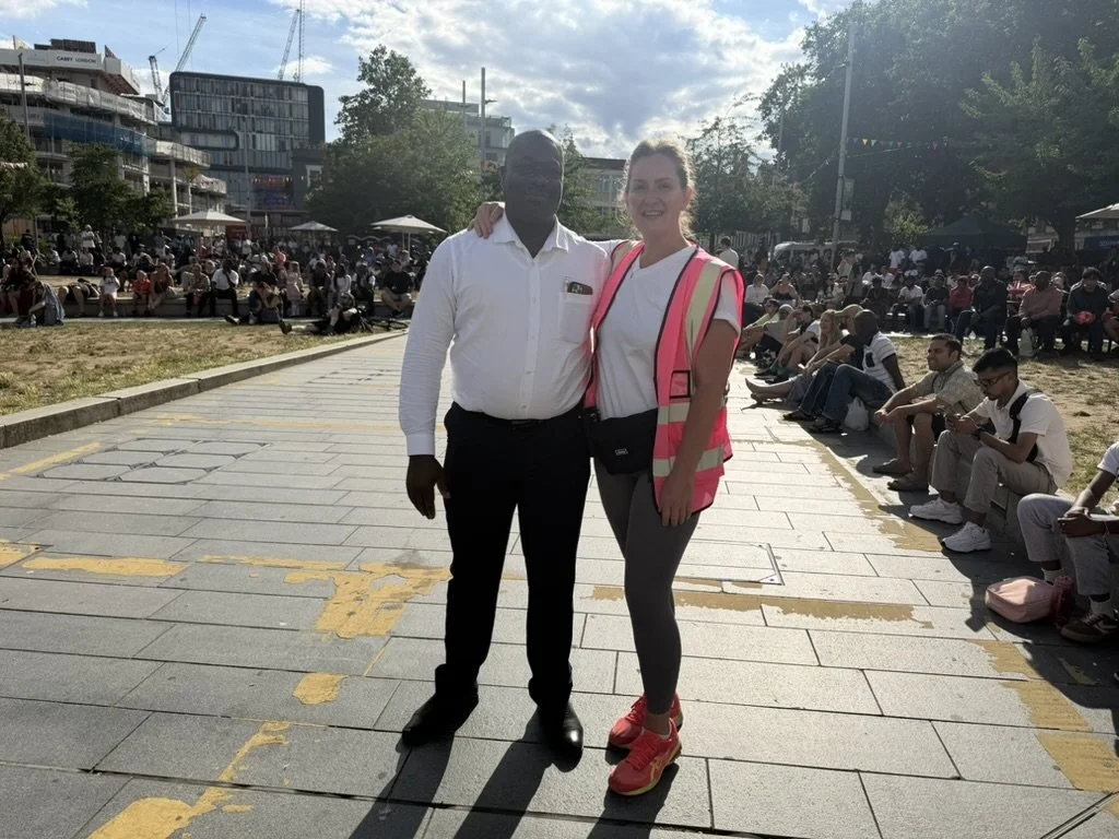Layla in a pink high vis vest with a colleague in front of the crowd