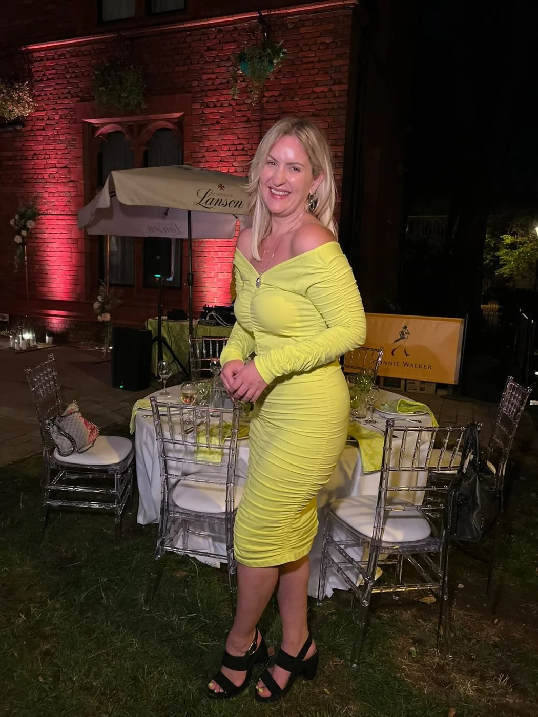 Layla smiling beside a dressed table in the courtyard lit pink for the evening
