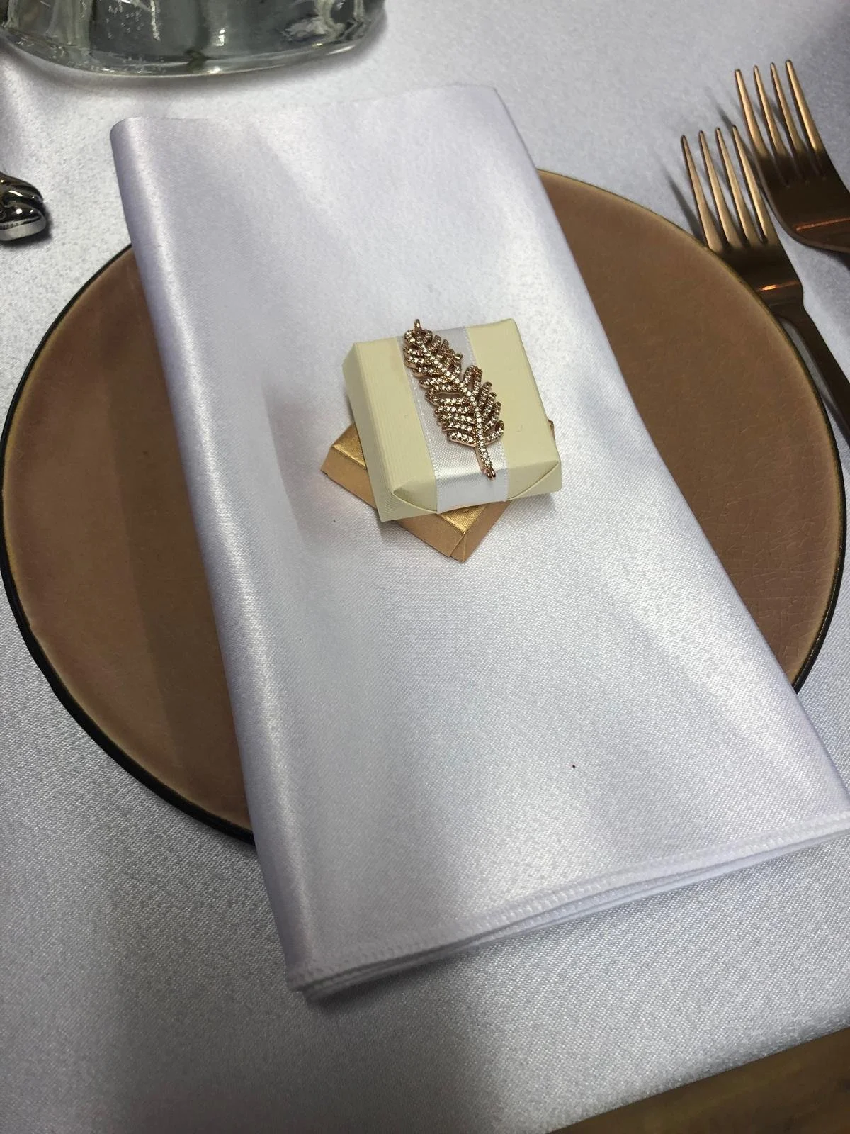 A wrapped favour with a jewelled feather on a folded satin napkin