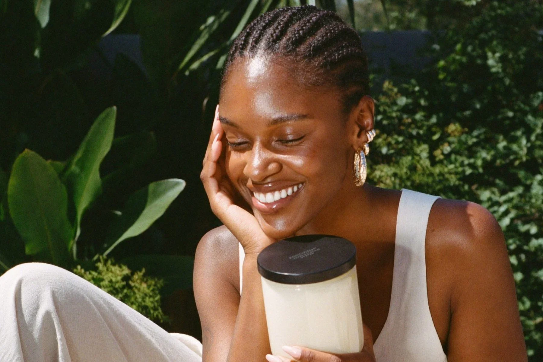 A smiling woman with glowing, moisturized skin holding a jar of body butter