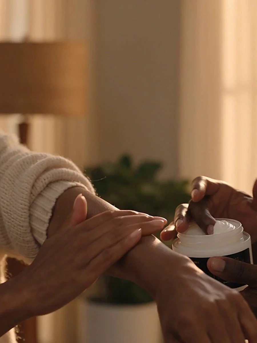 Hands smoothing body butter onto an arm, with an open jar held nearby