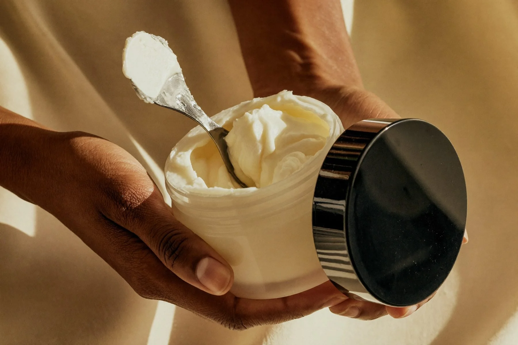 Hands scooping whipped body butter from a jar