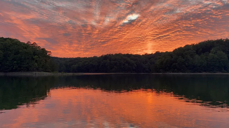 Coral-red sunset sky and fire-colored reflection across Laurel River Lake photographed by Rachel Stepek