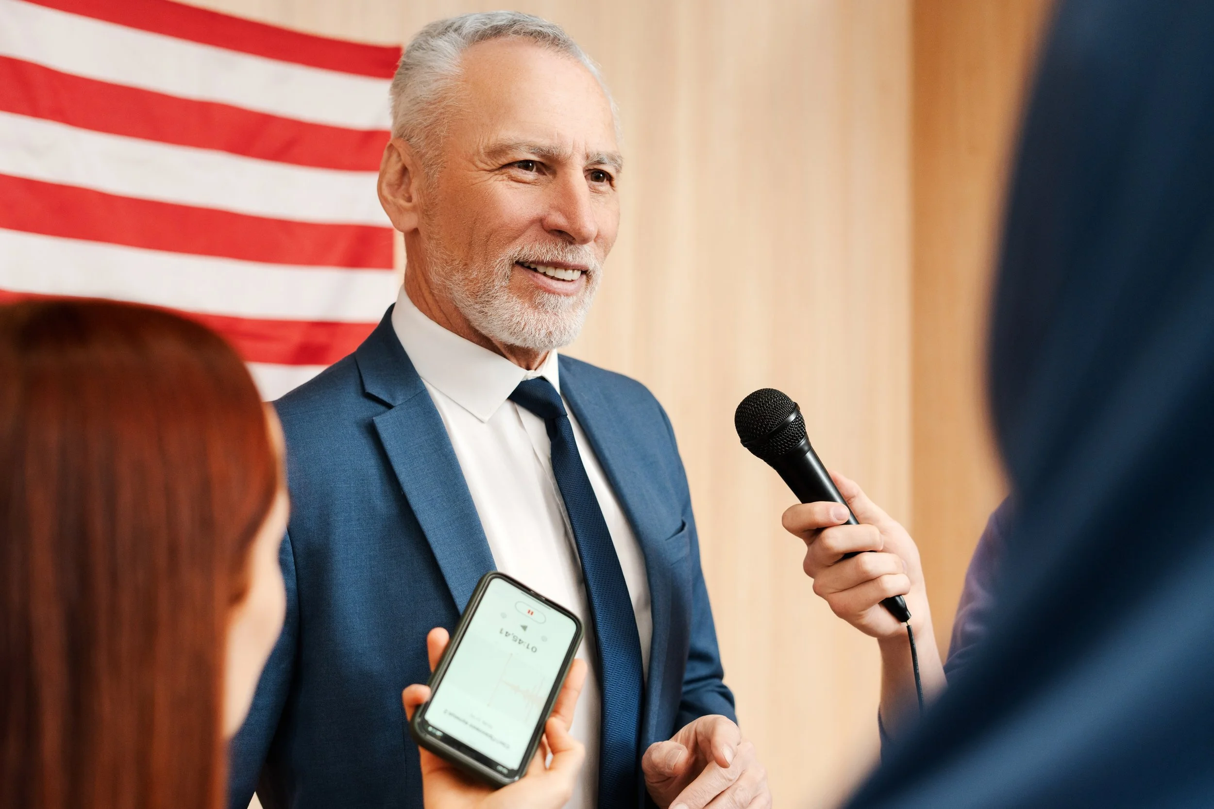 Man being interviewed with American flag in background
