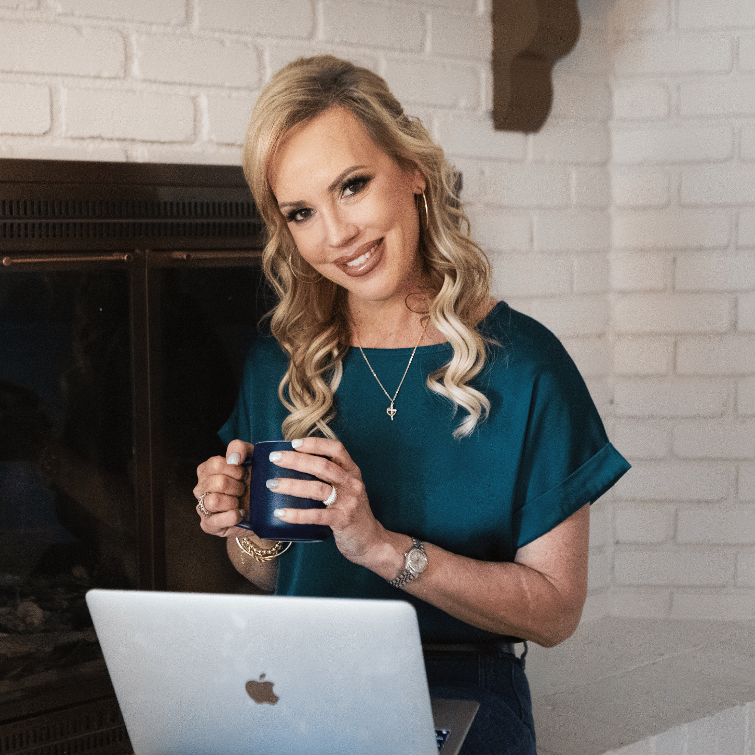 Sarah Engelhardt holding a mug and smiling at the camera with a laptop in front of her