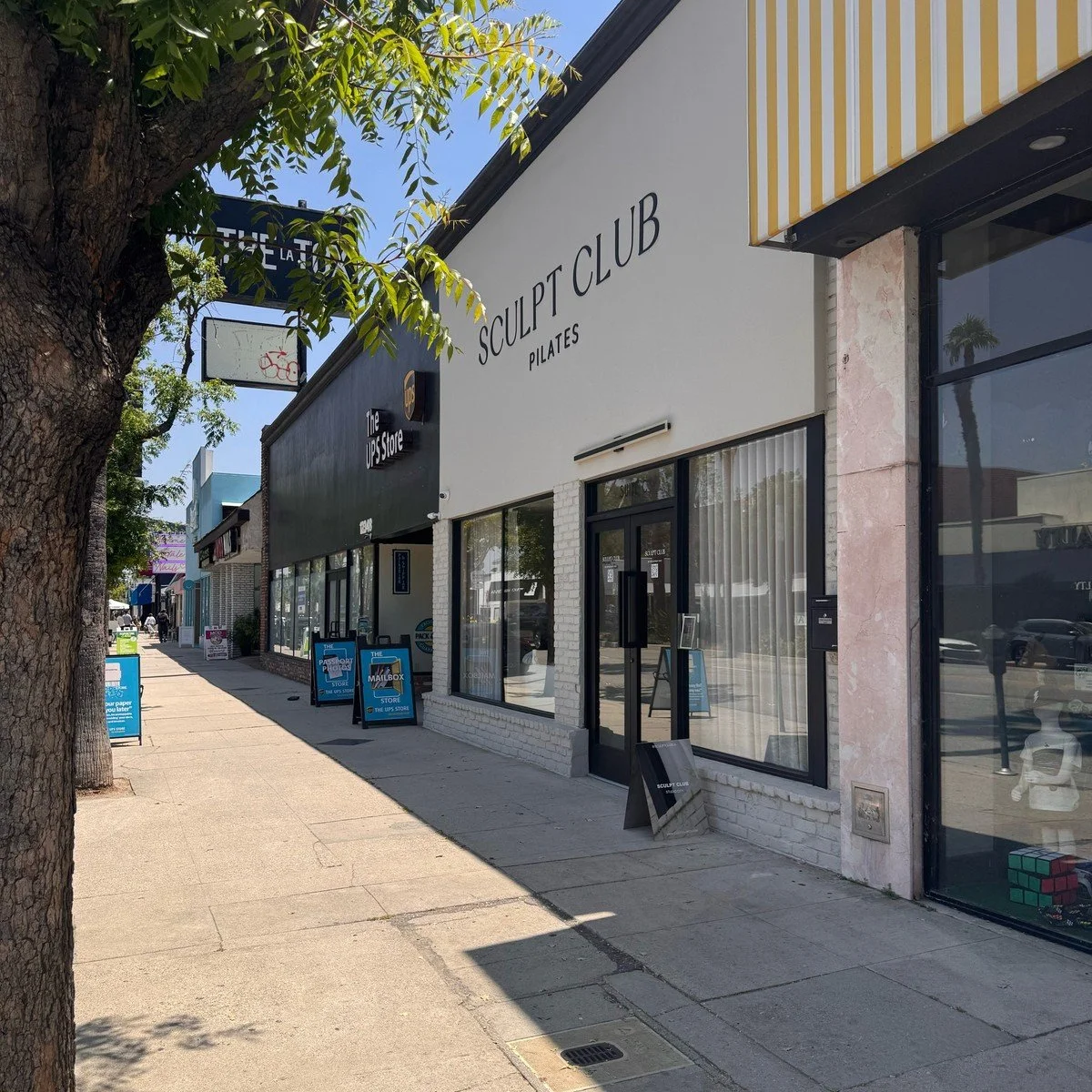 Sculpt Club Pilates and shops along a tree-lined Ventura Boulevard sidewalk in Studio City