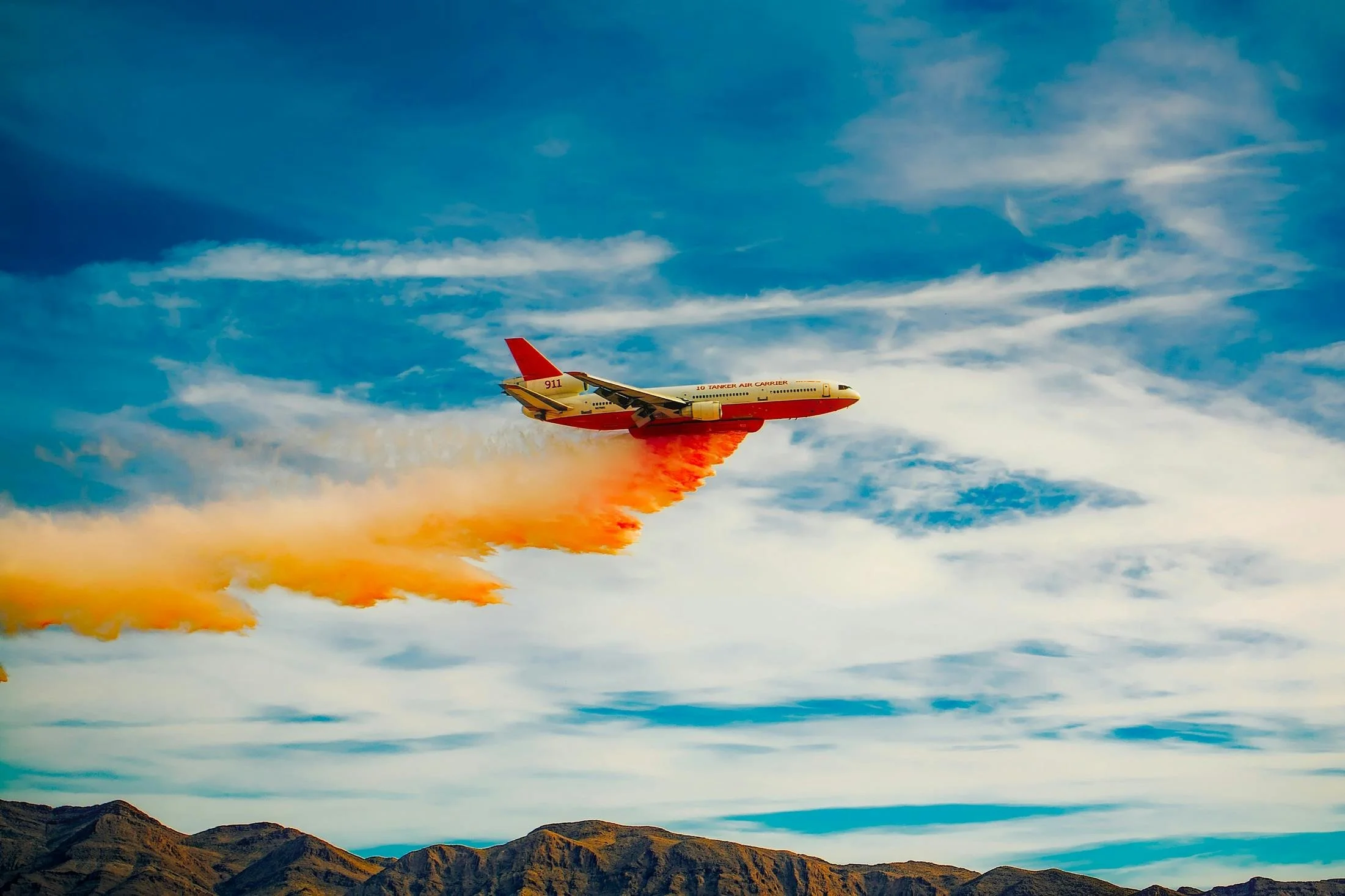 Airplane dropping fire retardant red slurry over forested hillside