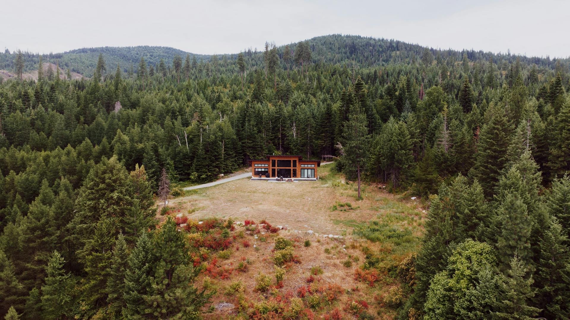 Aerial view of a modern mountain home surrounded by Northern Idaho conifer forest — the wildland-urban interface property type that drives Montana home insurance carrier risk-score analysis under HB 533.