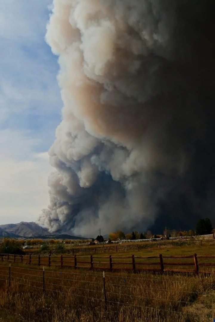 A Montana home in wildland-urban interface terrain under wildfire-season conditions, smoke on the ridgeline
