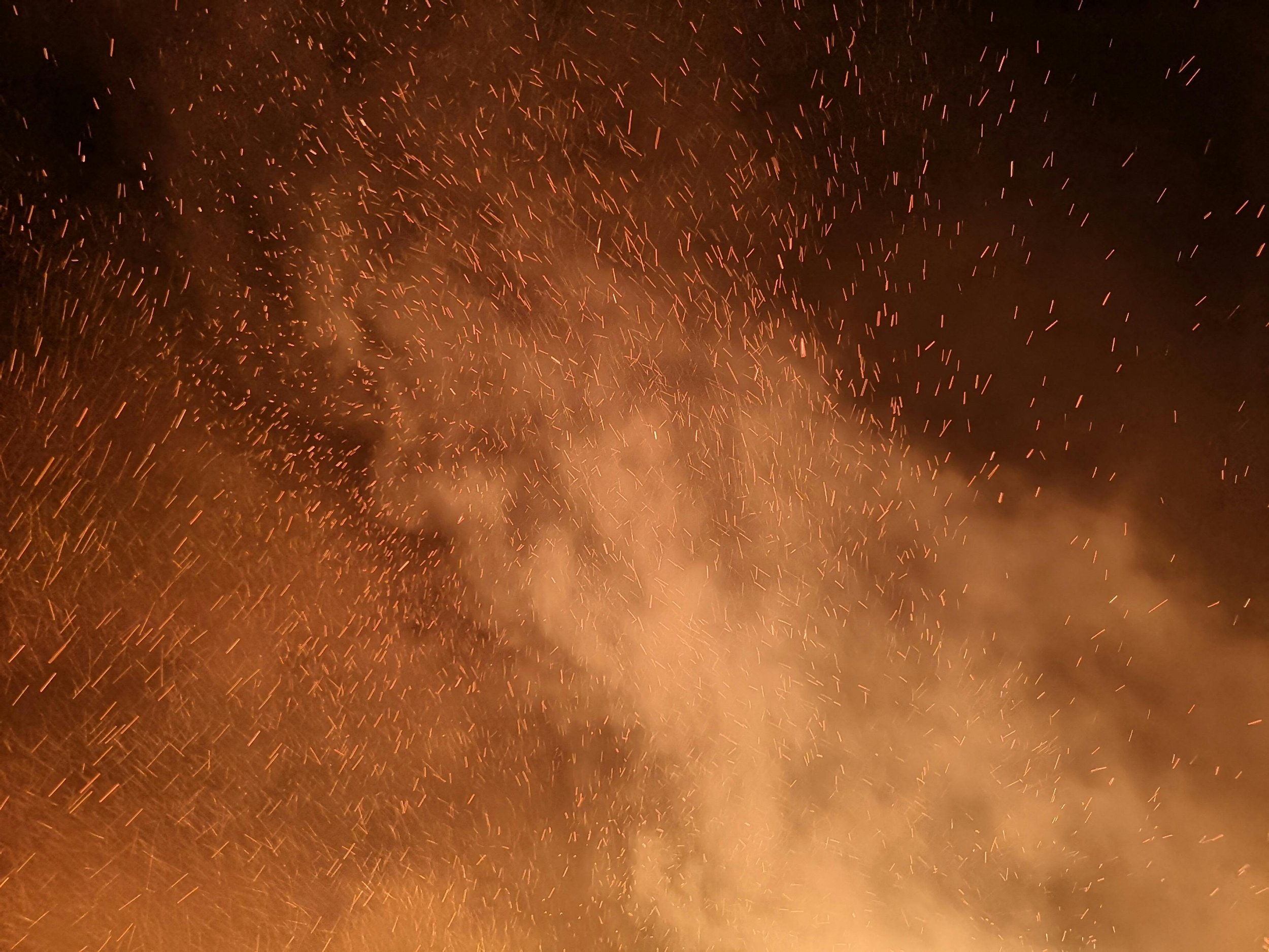 Wind-driven wildfire embers glowing against a dark sky — the primary way fire reaches and ignites homes