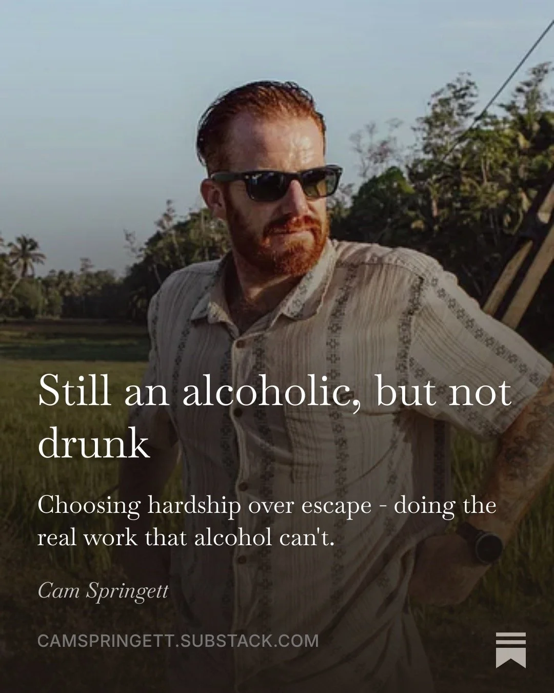 Still an alcoholic, but not drunk. Choosing hardship over escape, doing the real work that alcohol can't. Cam Springett in sunglasses standing in a sunlit green field.