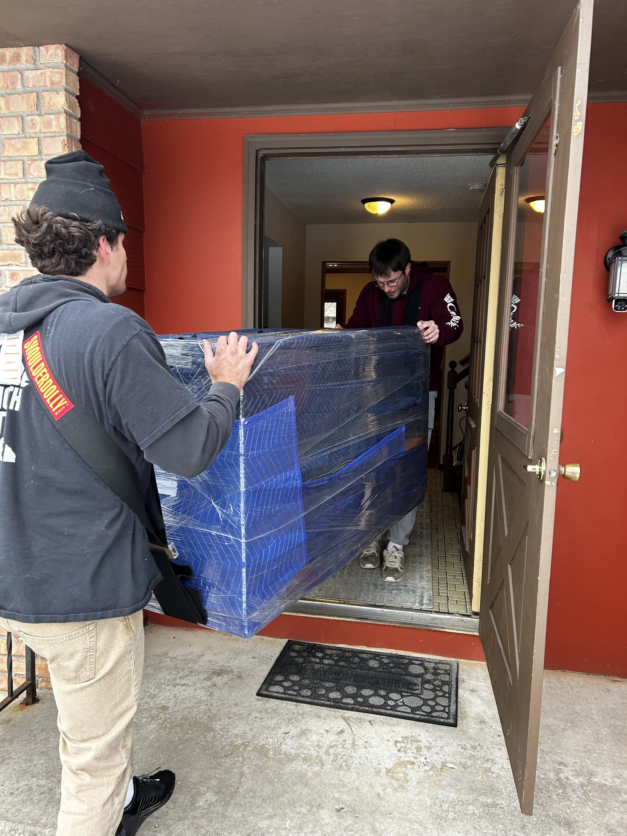 Collegiate Power Movers crew carrying wrapped furniture through a home entrance