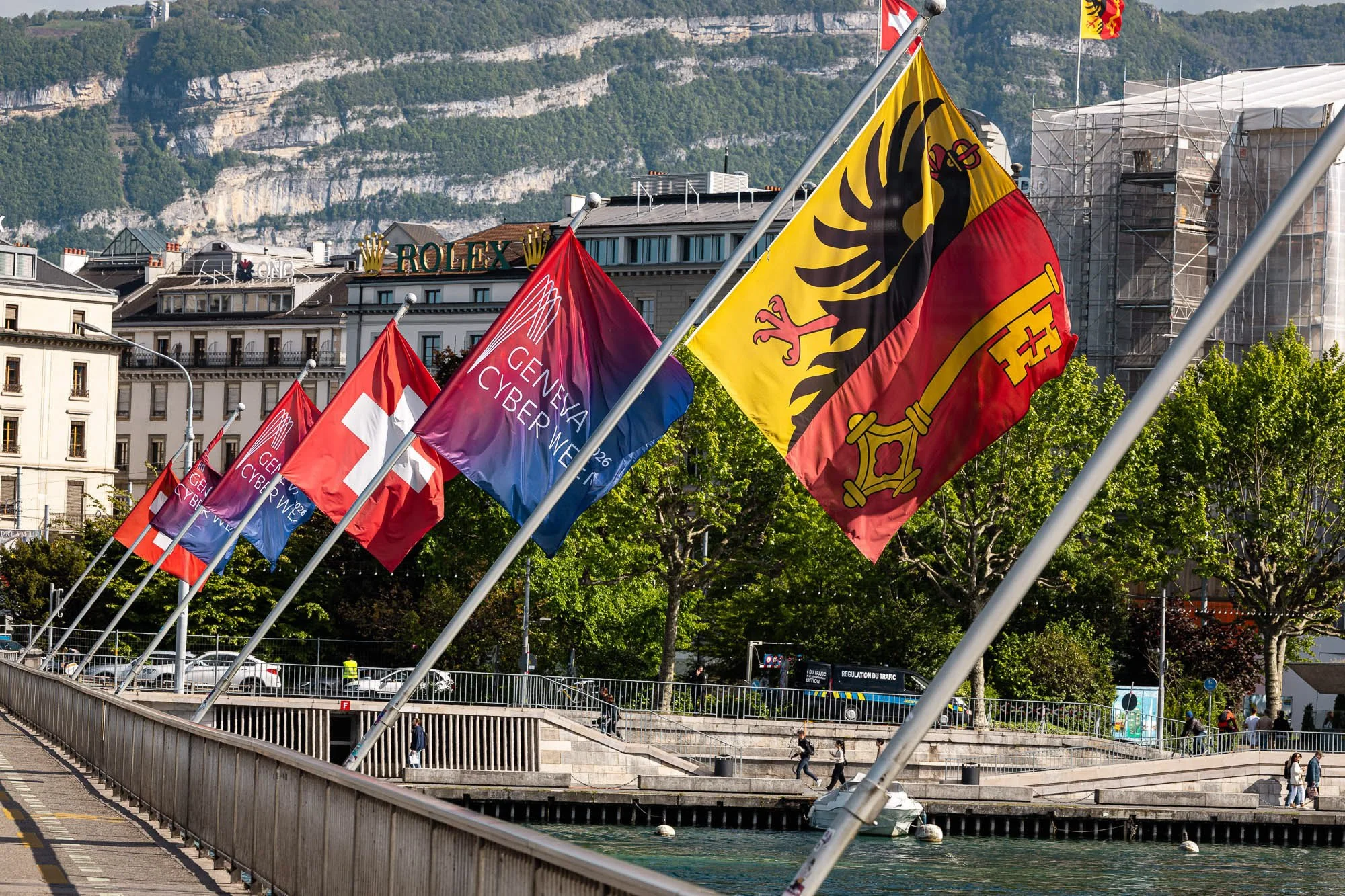 Geneva Cyber Week, Swiss, and Geneva flags lining the Pont du Mont-Blanc beside the water.