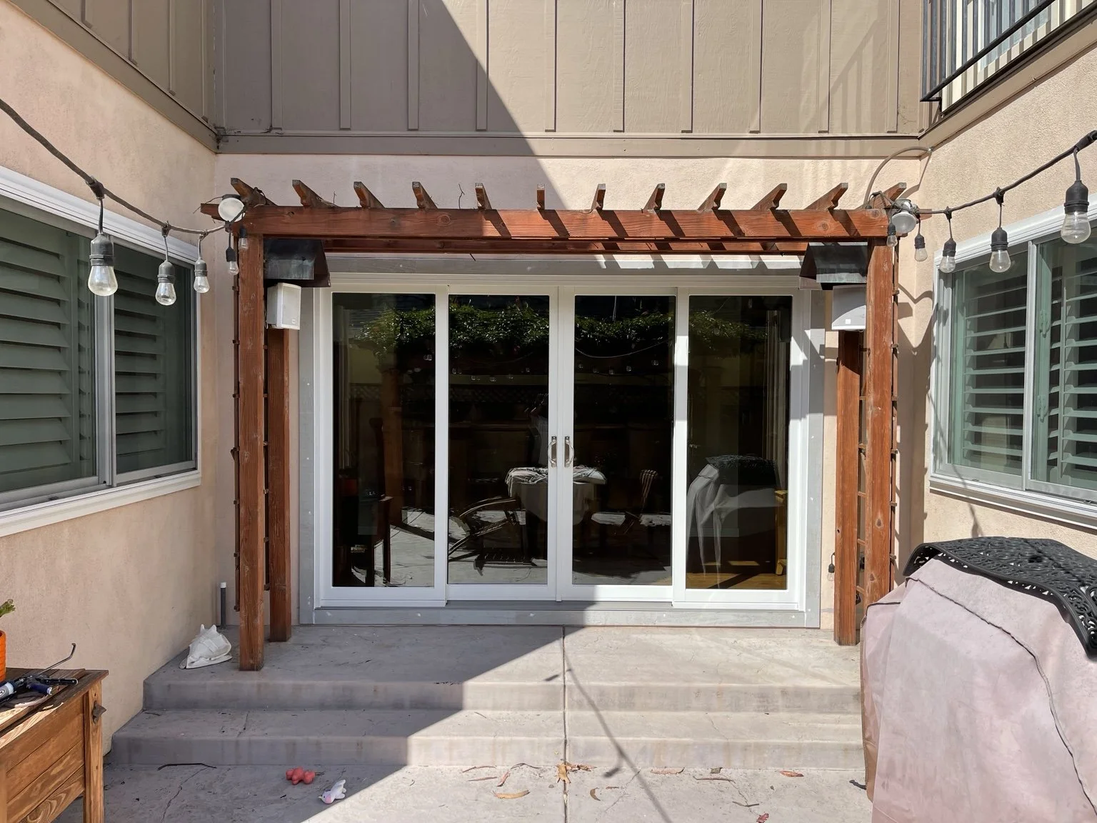 White patio doors beneath a wood pergola, with windows on either side