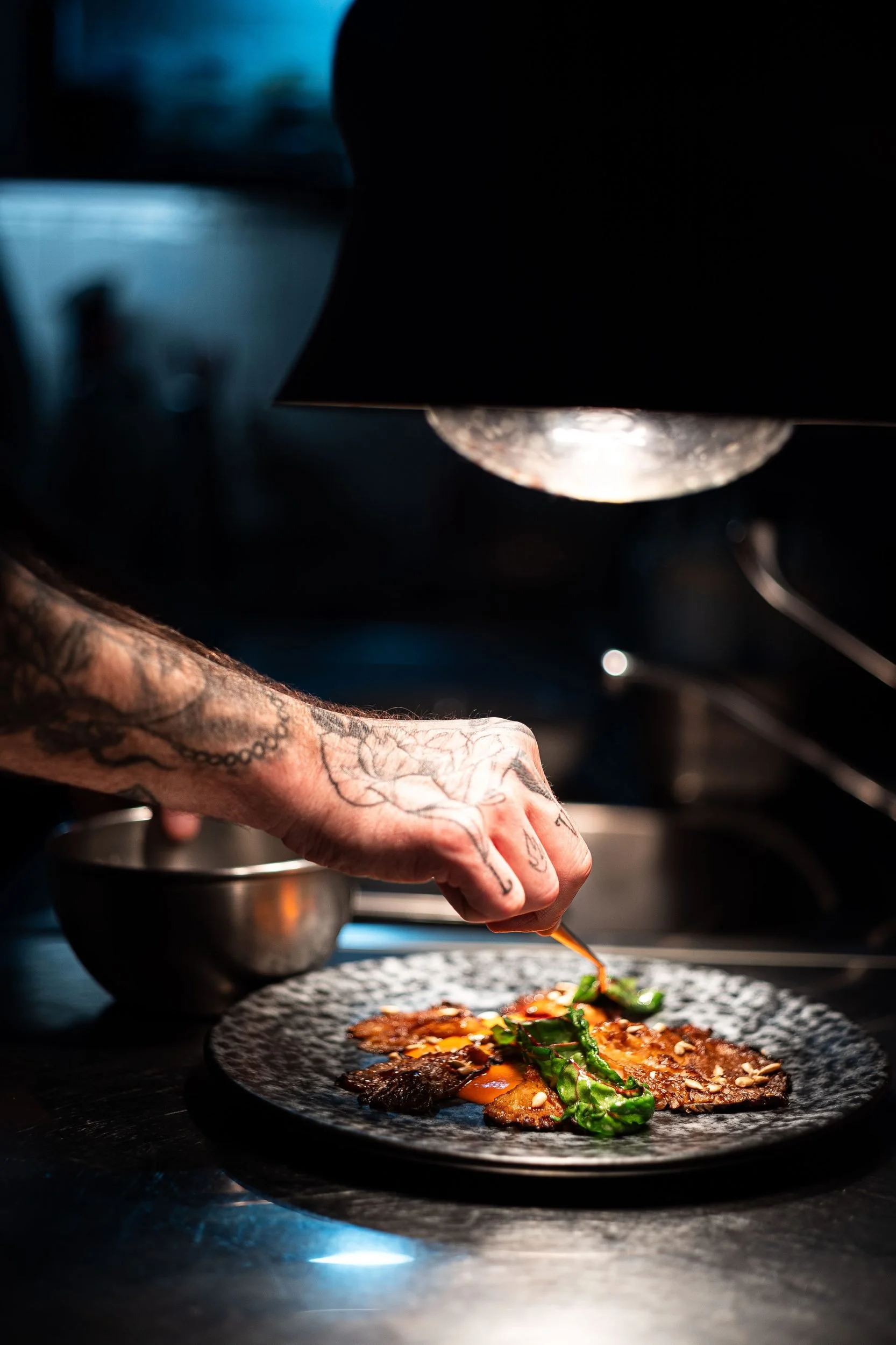 Chef tattooed hand finishing meat dish