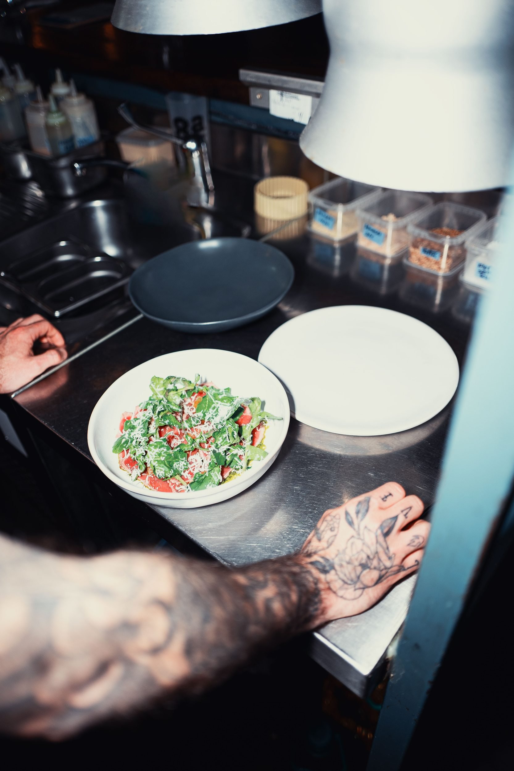 Chef tattooed hands plating salad