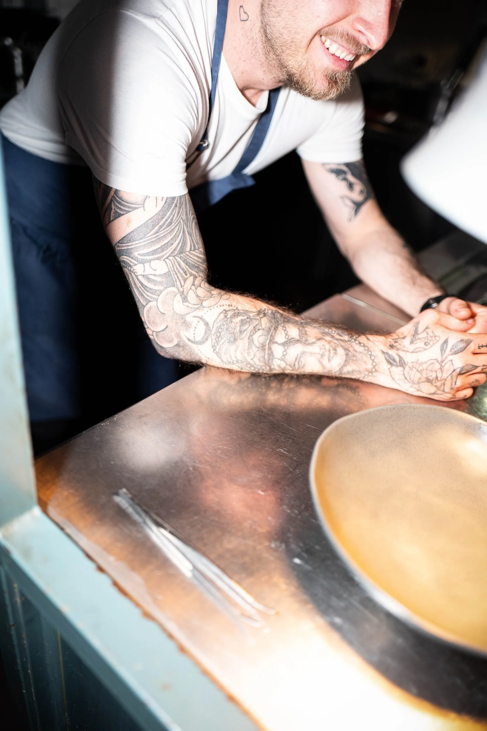 Chef tattooed arms leaning counter laughing