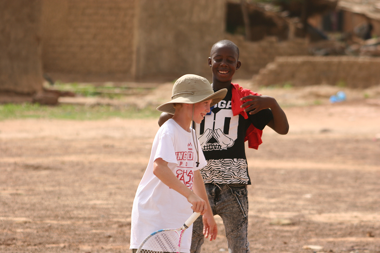 Two smiling young people standing together on an earthen playing area in Mali
