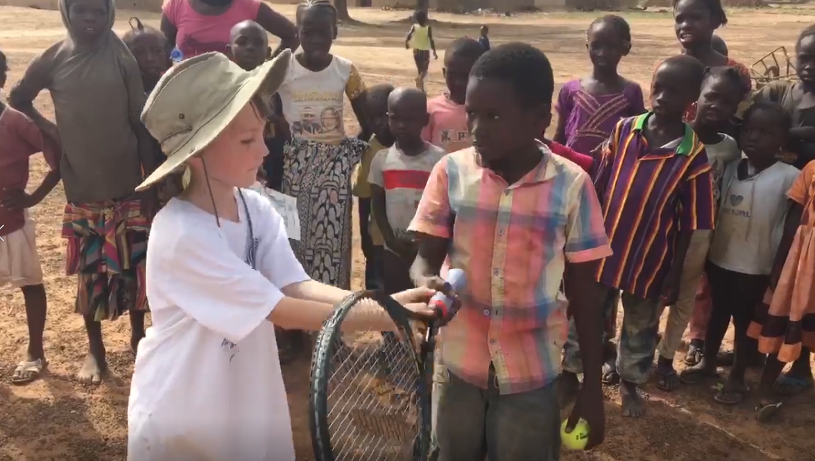 A volunteer and young player holding a racket as a group watches in Mali