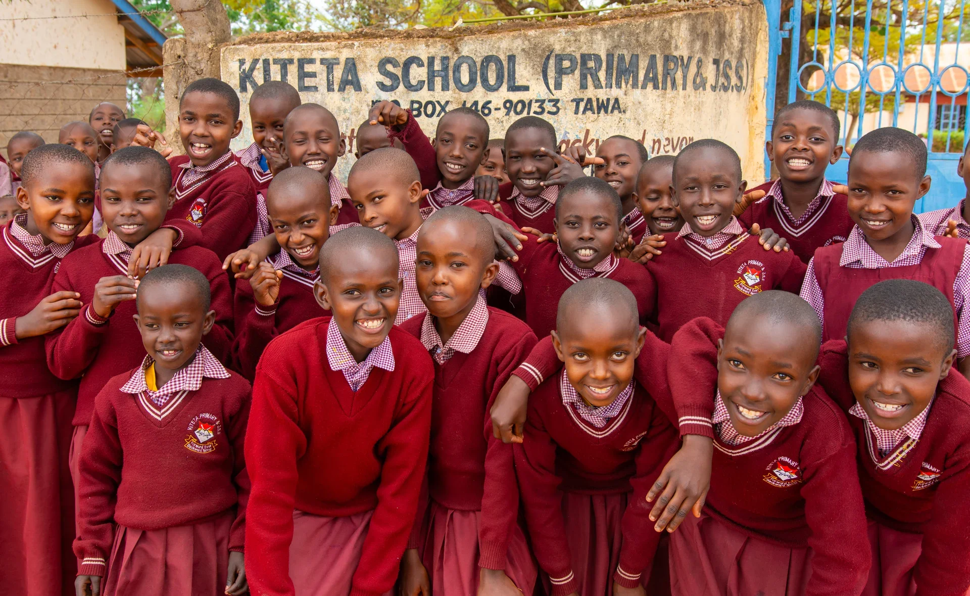 Group of Kiteta Primary School students smiling together holding a sign.