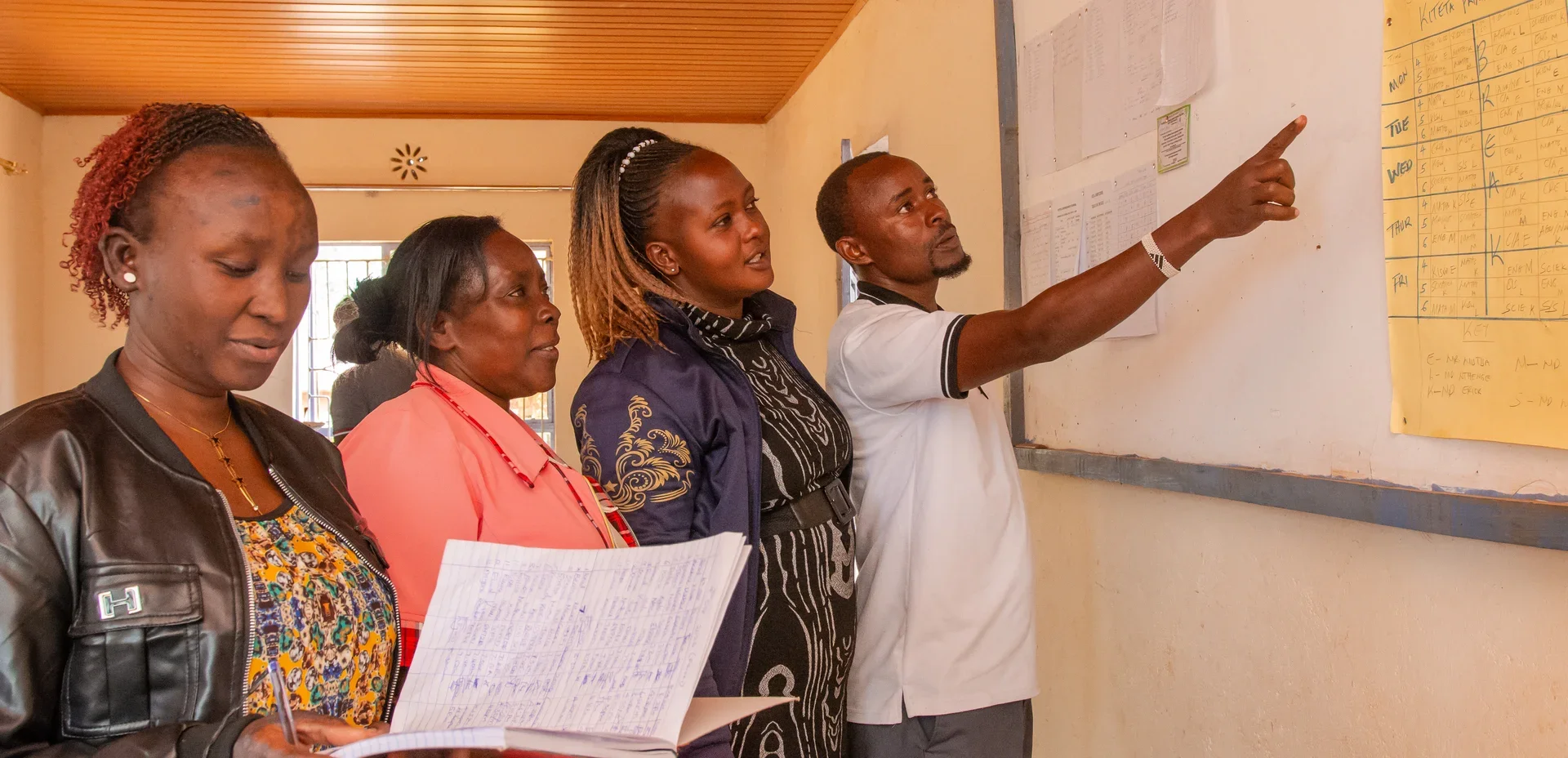 Kiteta Primary School staff gathered together reviewing an educational wall chart.