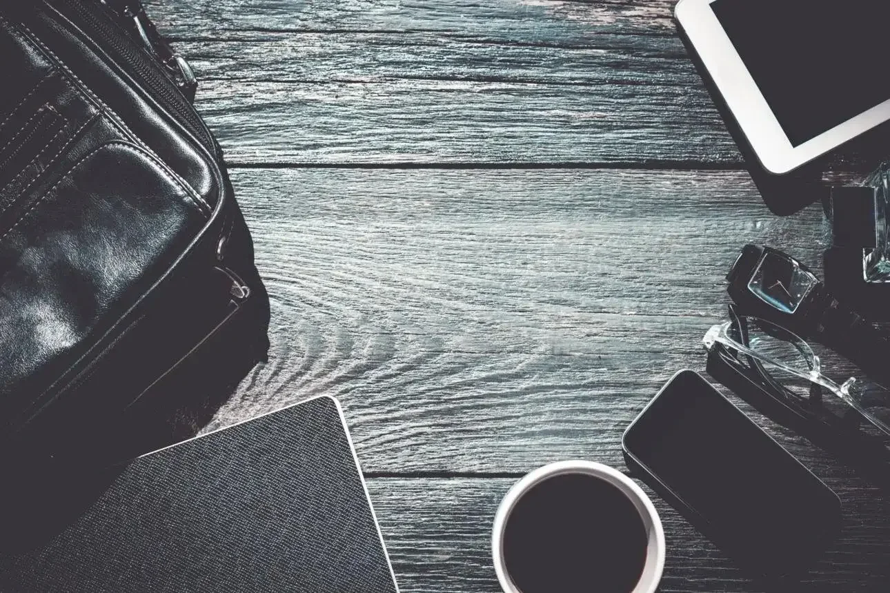 Father’s Day gift flatlay with leather bag, coffee, notebook, phone, watch, glasses, and tablet on a dark wood desk