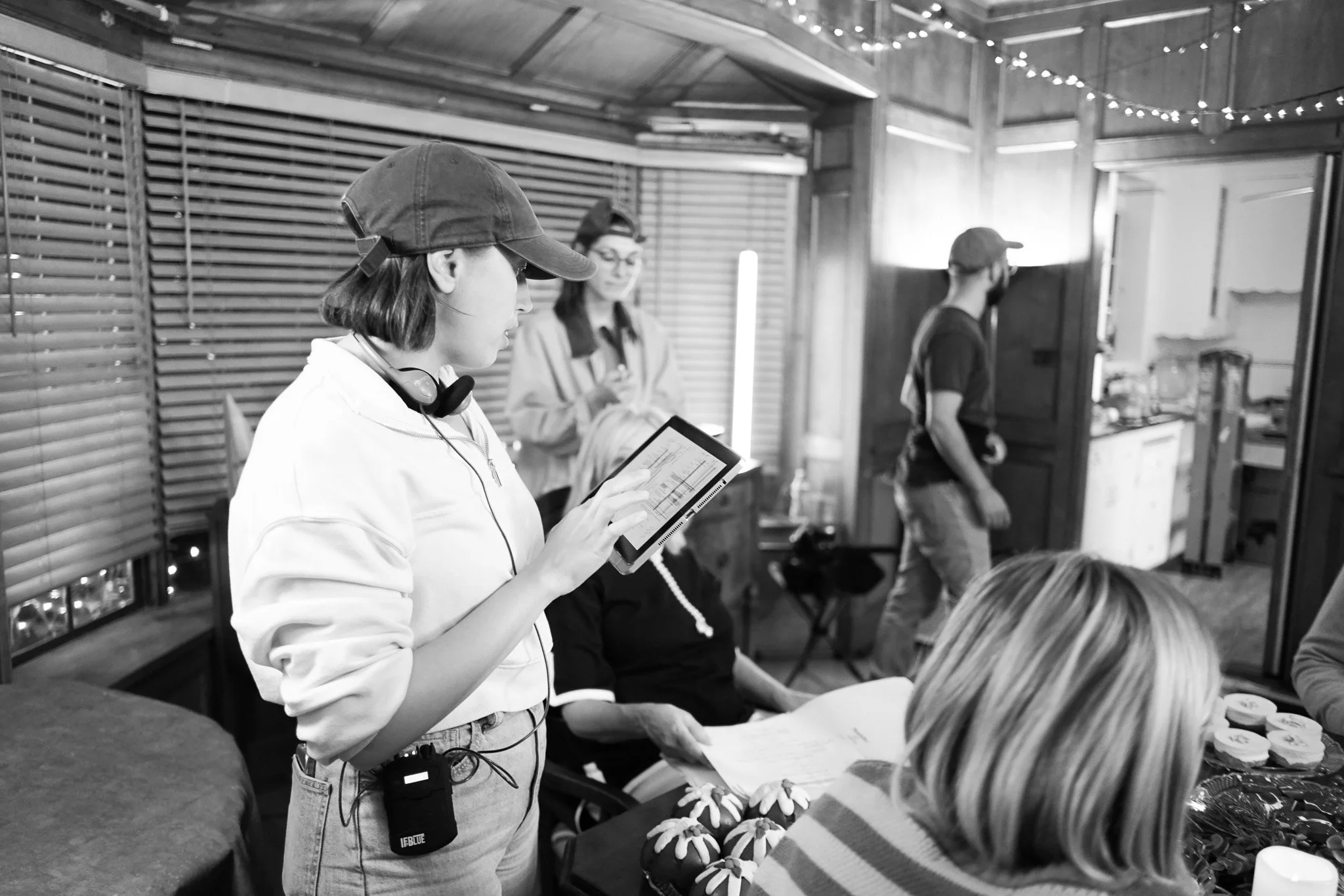 Production still: a director in a pink headband directs a scene on a colorfully lit set.