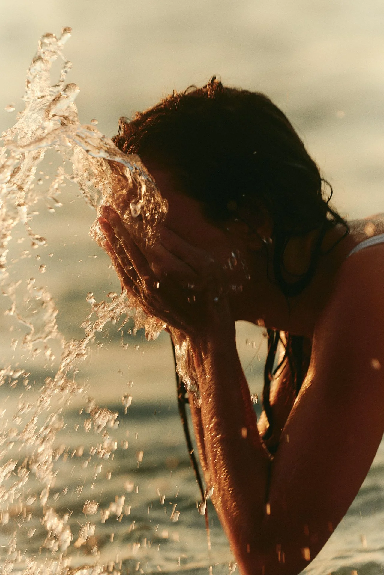 Woman splashing water on face in ocean at golden hour for skin regeneration