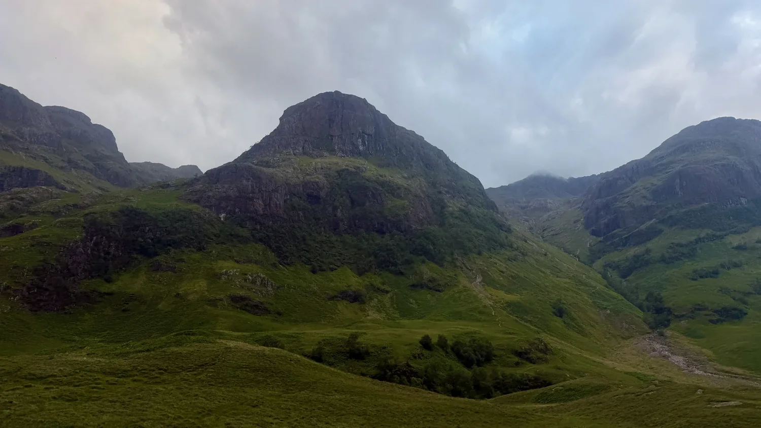 Steep green mountains rise above a quiet glen in Glencoe.