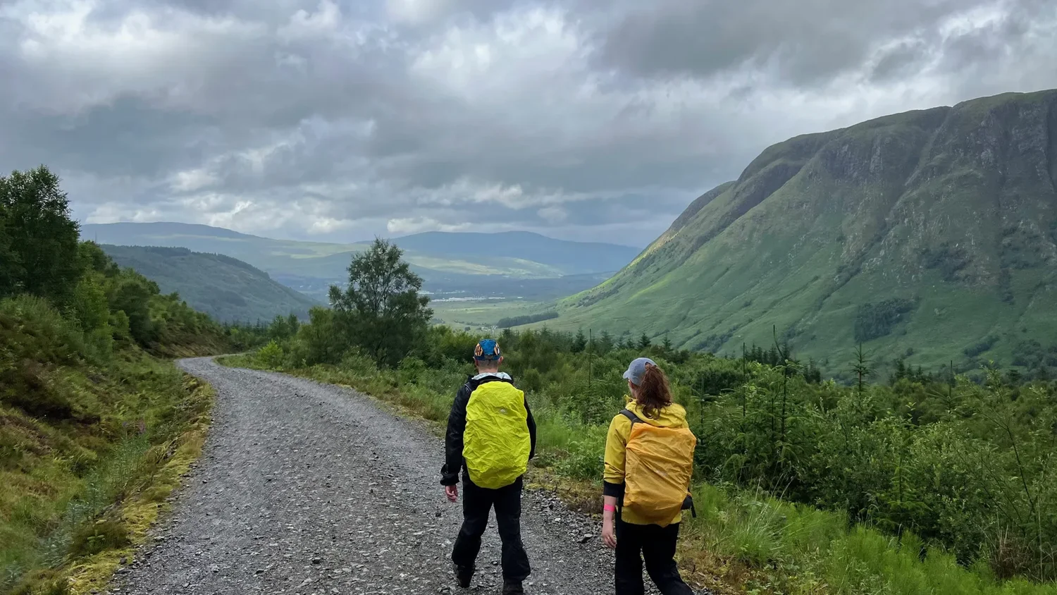 Two walkers head into a Scottish glen together, photographed from behind.
