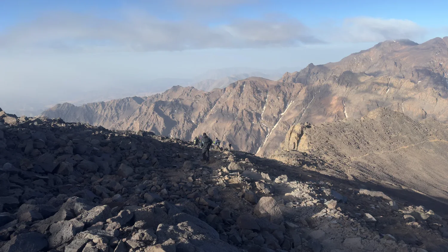 Distant walkers follow rocky terrain above successive ridges in the Atlas Mountains.