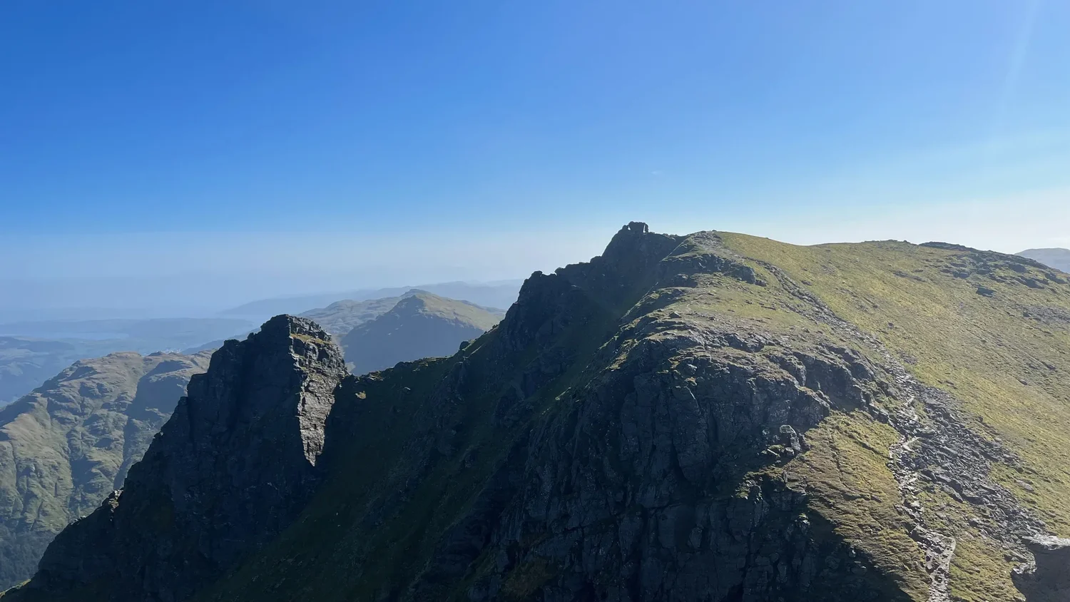 Rocky summits and a sunlit ridge above Arrochar, with Scottish hills stretching into the distance.