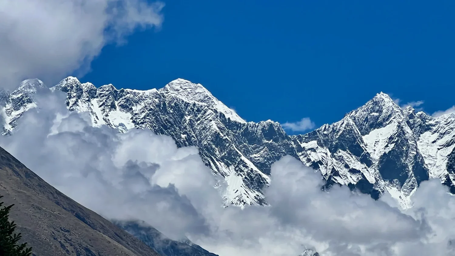 Snow-covered Himalayan peaks rise above cloud beneath a deep blue sky.