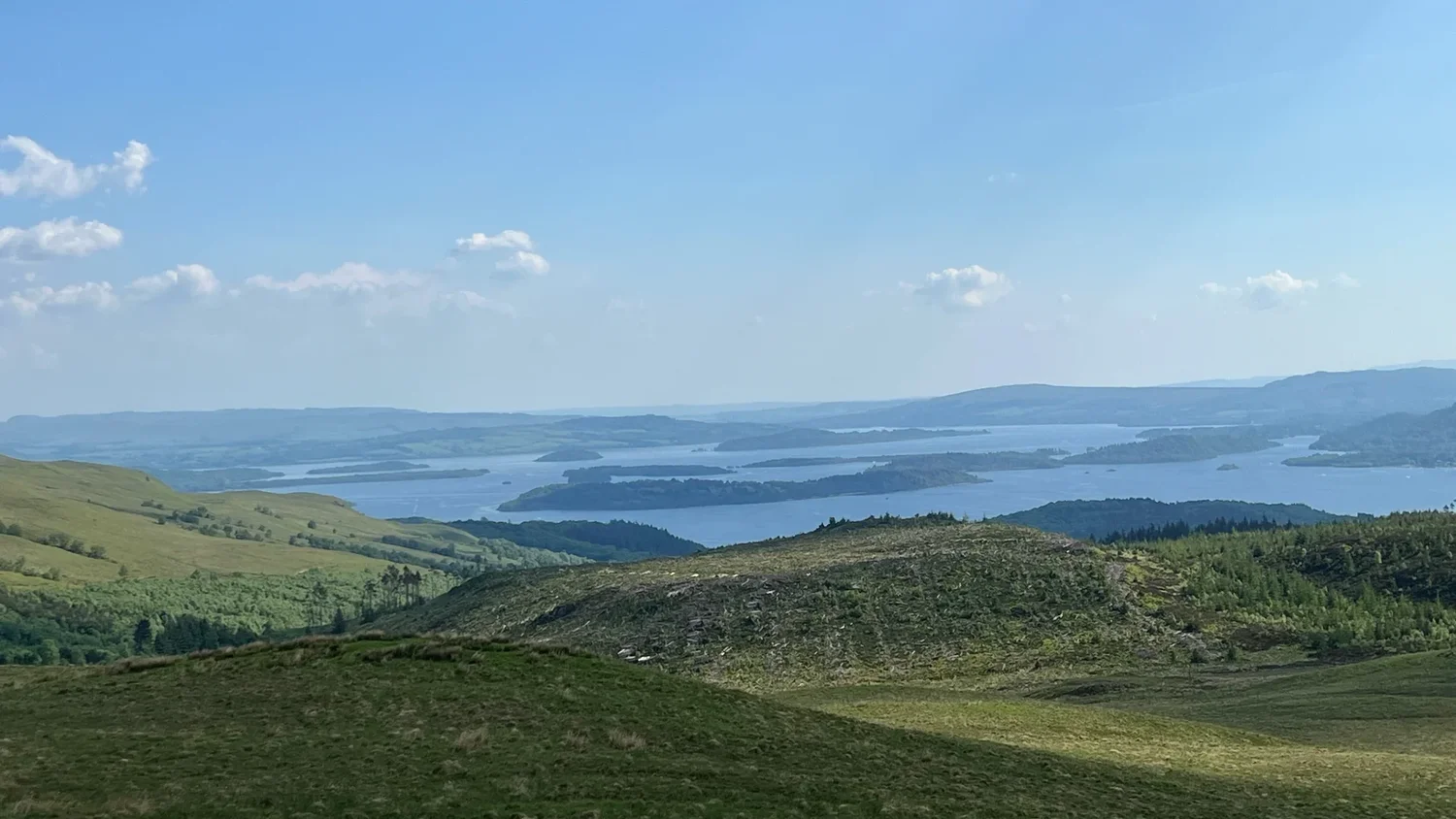 Open green slopes on Ben Lomond look across Loch Lomond towards the distant horizon.