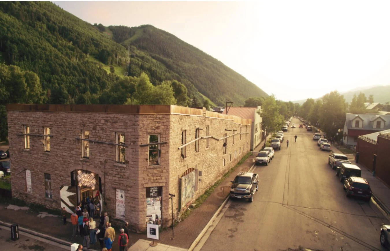 A summer evening crowd gathering outside the Transfer Warehouse in Telluride, golden light, Box Canyon mountains rising behind