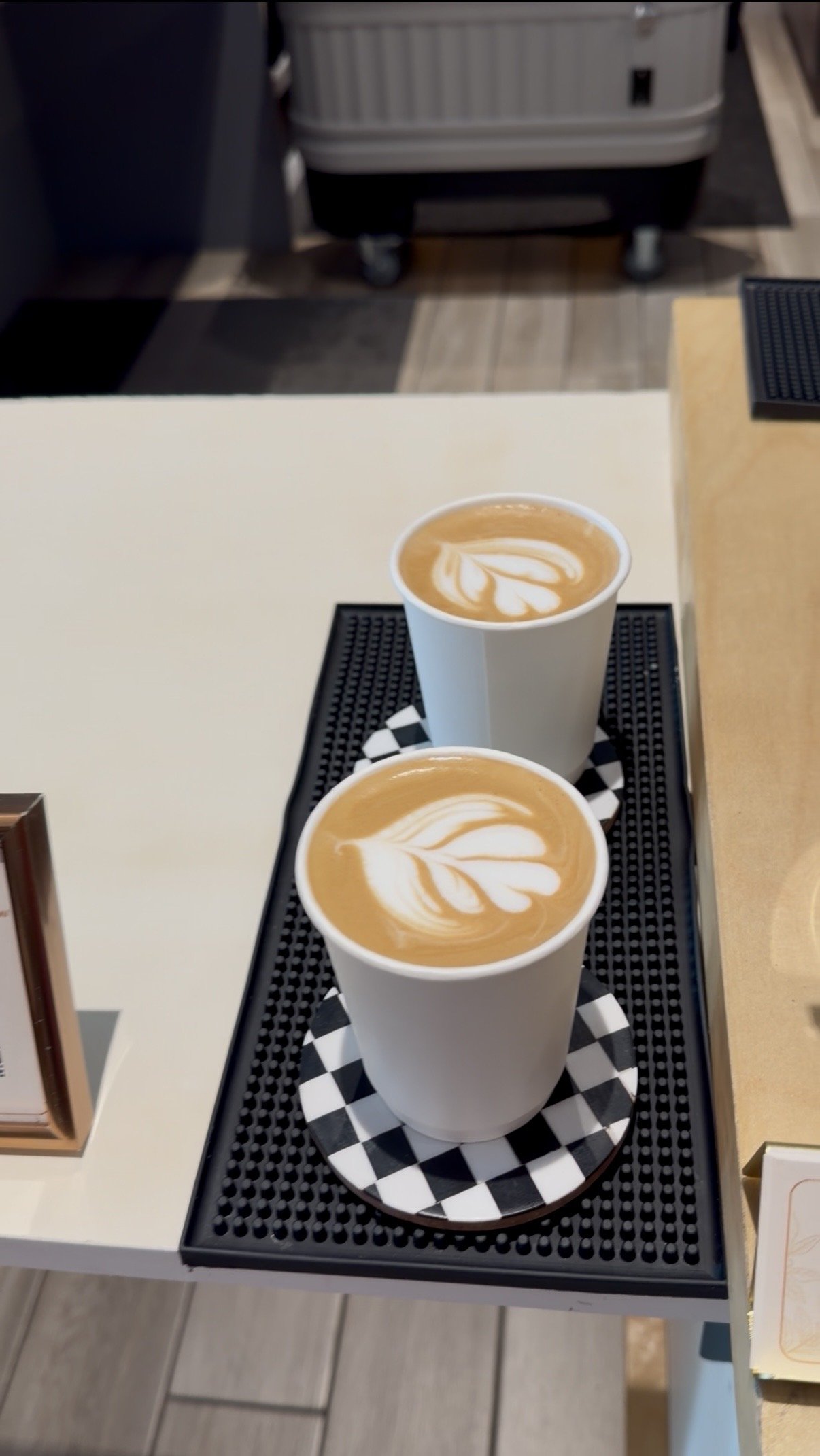 Two lattes with latte art on checkered coasters at a Goldcrest Brew corporate coffee cart