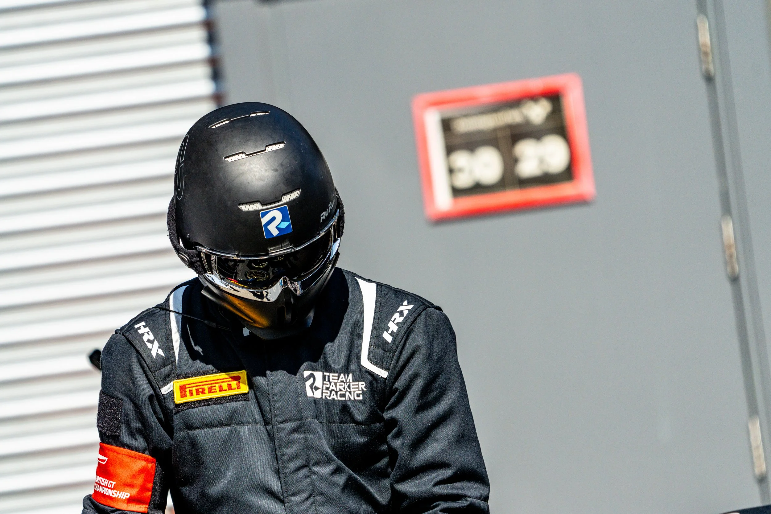 Helmeted racing driver preparing beside the garages