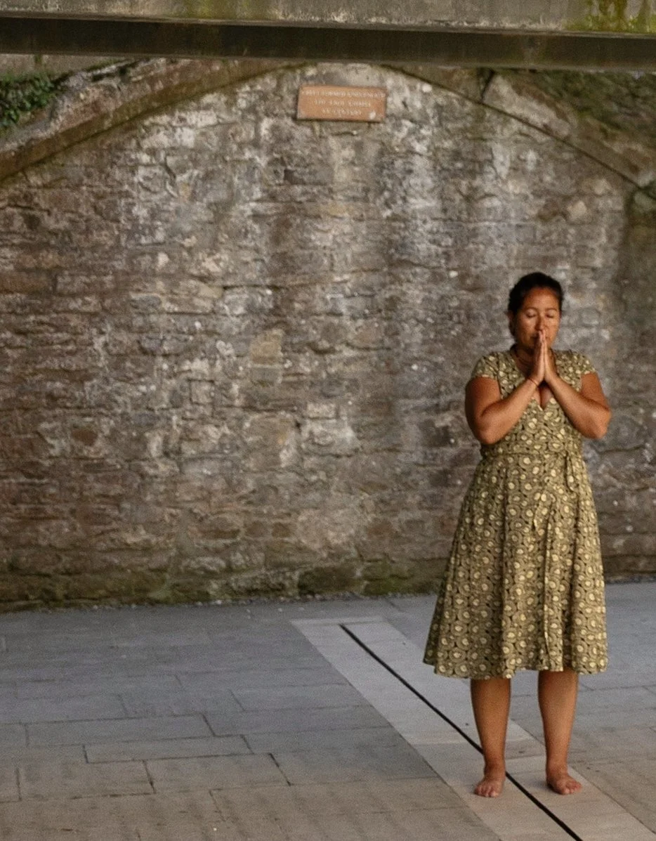 Marielly standing barefoot in quiet prayer before an old stone wall