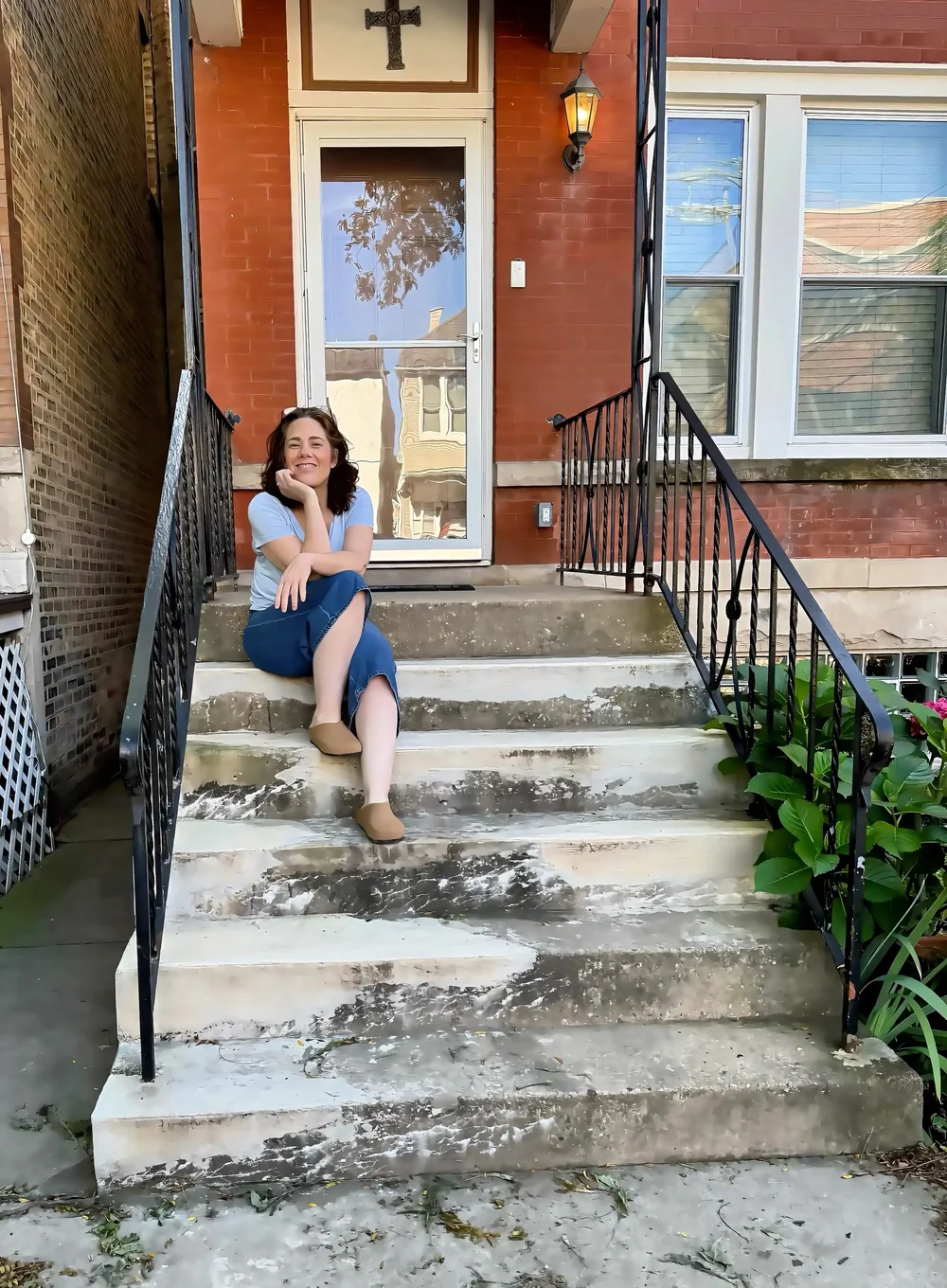 Briana Watson sitting on the front steps of a Chicago two-flat, smiling toward the camera.