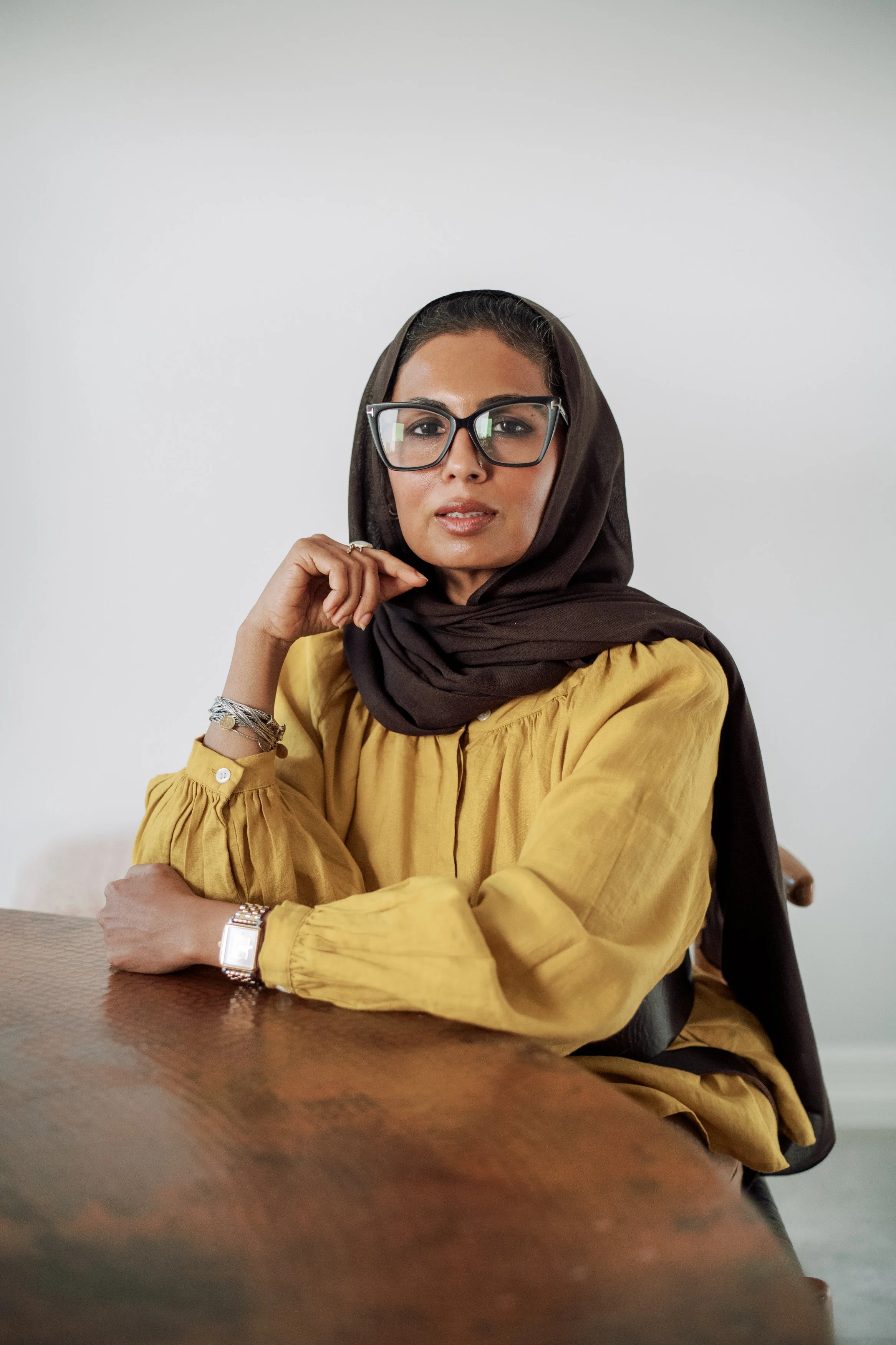 Dr. Farooqi seated at a wooden table in a dark headscarf